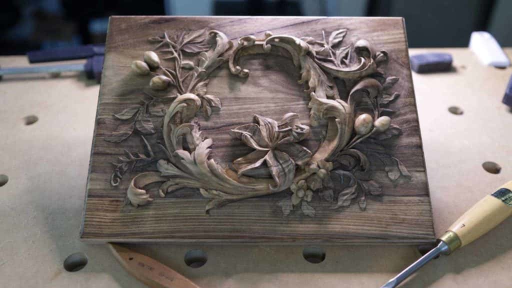A finished lily relief on a dark board whose grain lines show through the carving