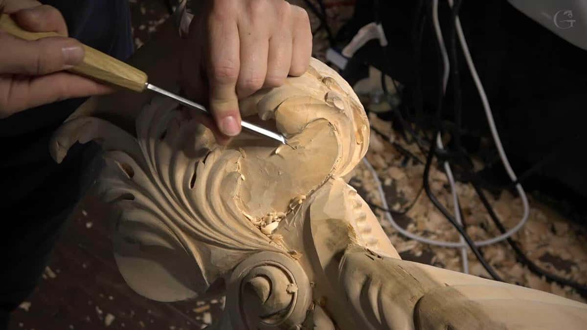 Close-up of a person carving intricate details into a wooden piece using a chisel. Shavings scatter around, showing the process of art in progress. Perfect for anyone looking to join wood carving classes or lessons!