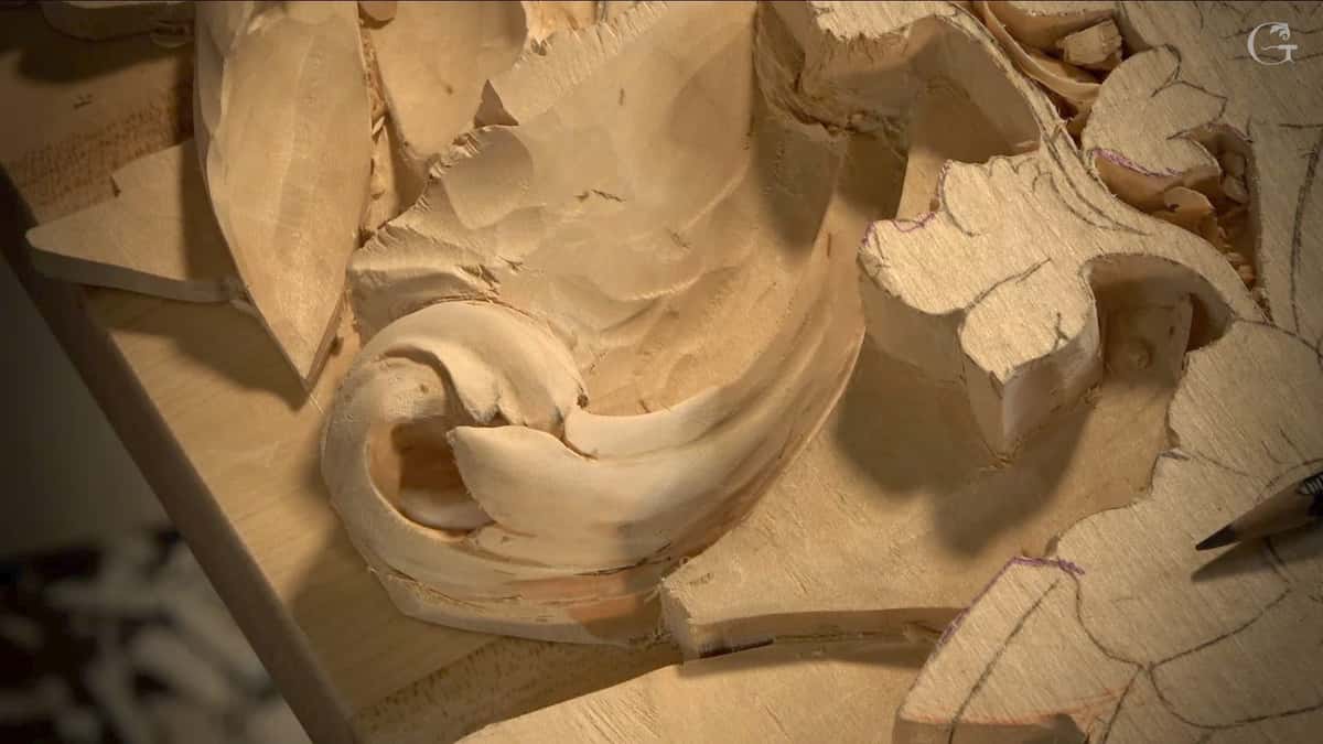 Alt text: Close-up of a wood carving project in progress, showcasing intricate details of swirling shapes and moving strokes on light-colored wood. Nearby, a pencil lays against the wood, hinting at plans for wood carving lessons. This image captures the hands-on nature of wood carving classes and the artistry involved in creating unique wood designs.
