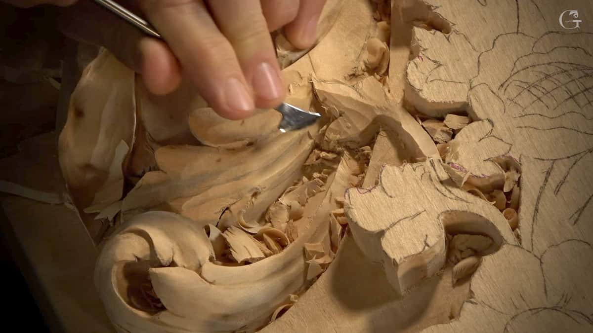 Close-up of a skilled wood carver using a small carving tool on a piece of wood. The intricate details of the design are becoming visible, with wood shavings scattered around. This scene captures the process of creativity in wood carving, perfect for anyone interested in wood carving classes or lessons!