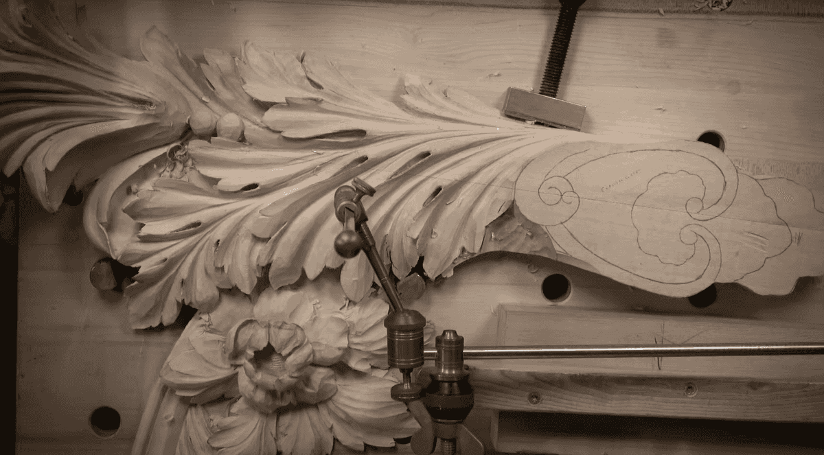 Alt text: Detailed view of a carved wooden design featuring intricate leaf patterns, showcasing tools on a carving workbench. Perfect for those interested in wood carving classes and lessons.