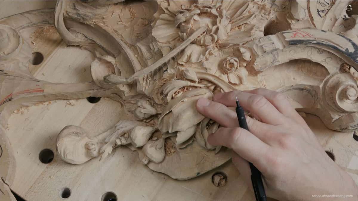 Close-up view of a hand holding a pencil, pointing at a meticulously crafted tulip flower featured on a Grinling Gibbons woodcarving. The woodcarving masterpiece showcases the detailed craftsmanship of woodcarving. Grinling Gibbons' woodcarving techniques are evident in the intricate design. The pencil underscores the precision involved in woodcarving. Tulip flower, a highlight of the woodcarving, depicts the realistic approach of Grinling Gibbons' woodcarving style. The woodcarving composition presents a harmonious blend of nature and art. An unmissable piece of woodcarving art demonstrating the timeless beauty of Grinling Gibbons' woodcarving legacy. The woodcarving reveals the artist's meticulous attention to detail. This woodcarving is a testament to the skills required in creating such intricate works of art. Explore the depth and texture of this stunning example of Grinling Gibbons' woodcarving prowess.