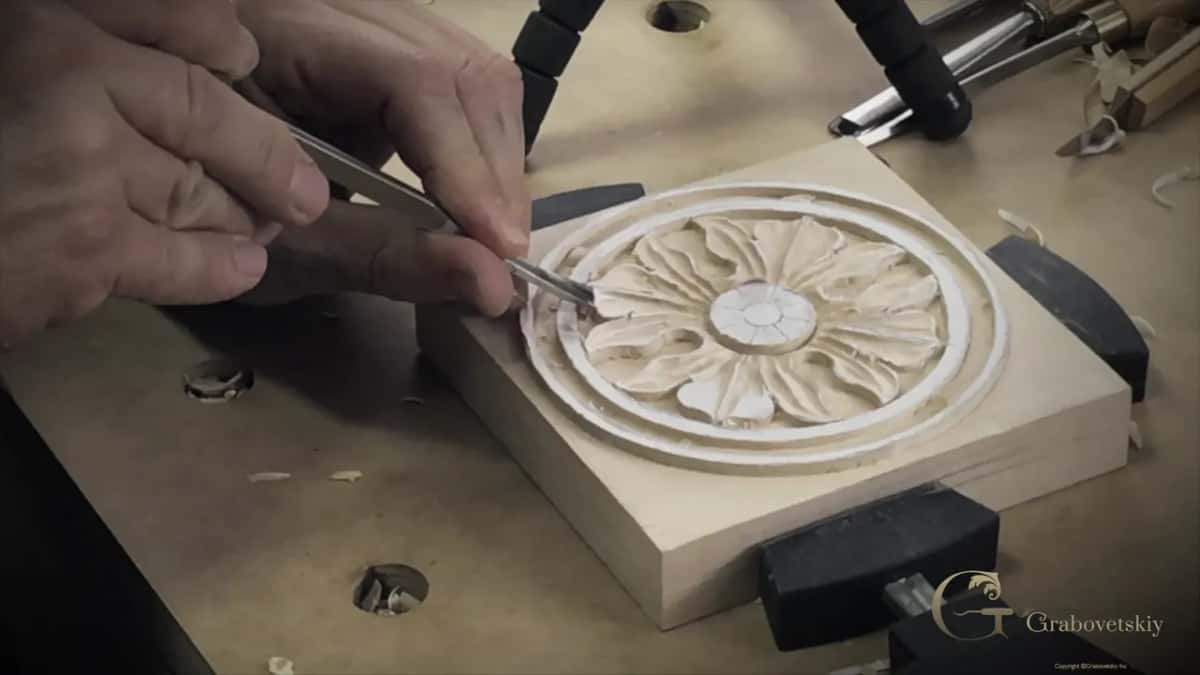 A round rosette of pointed petals clamped in bench dogs while both hands drive a chisel toward its center.