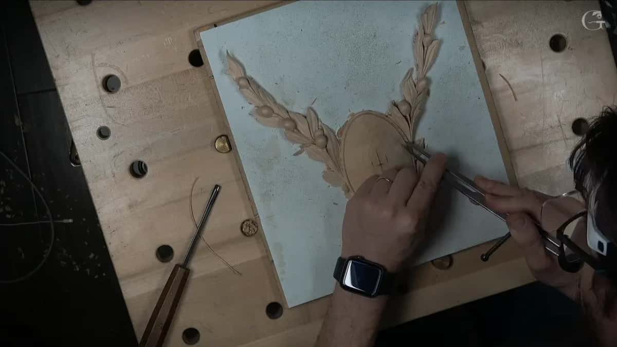 Both hands set dividers on the oval boss between two rising leaf sprays