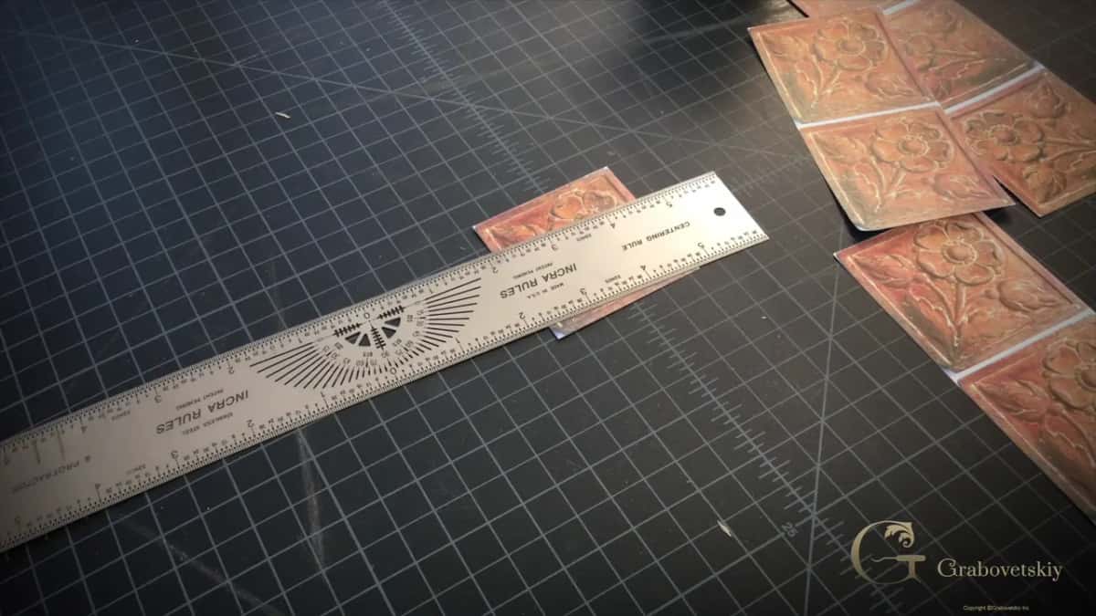 Nobody in frame: a long steel rule and a scatter of printed panel tiles resting on the gridded mat.