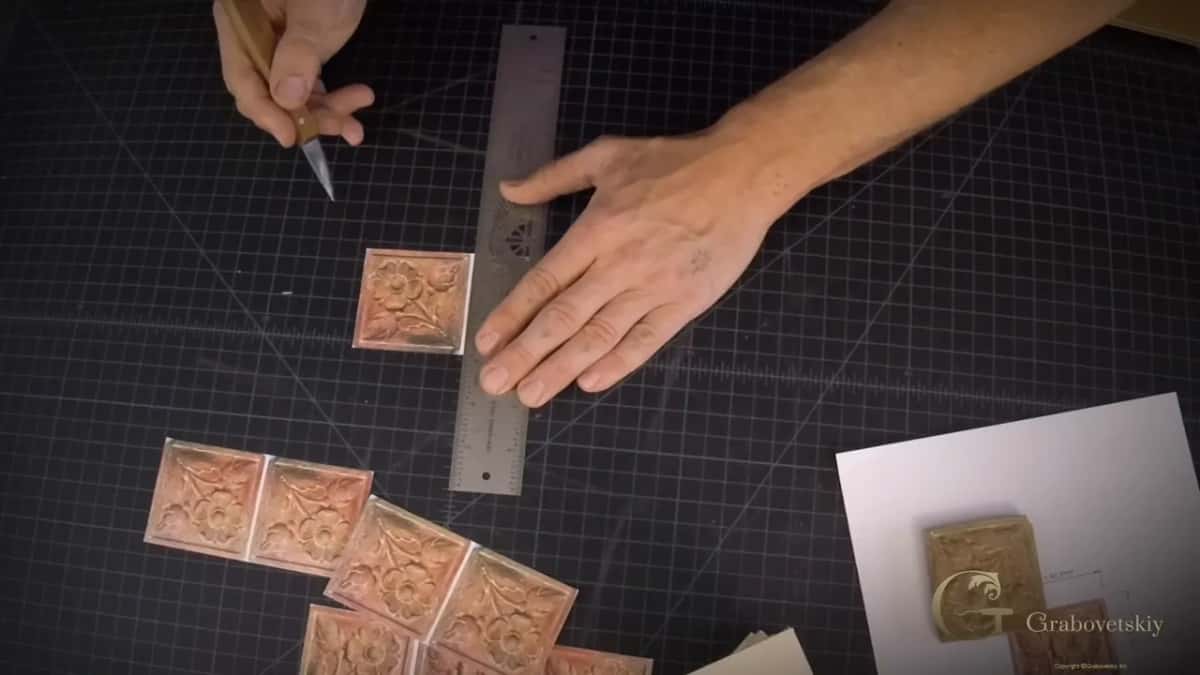Seen from overhead, a dozen printed flower tiles fan out across the mat beside a rule and a small blade.