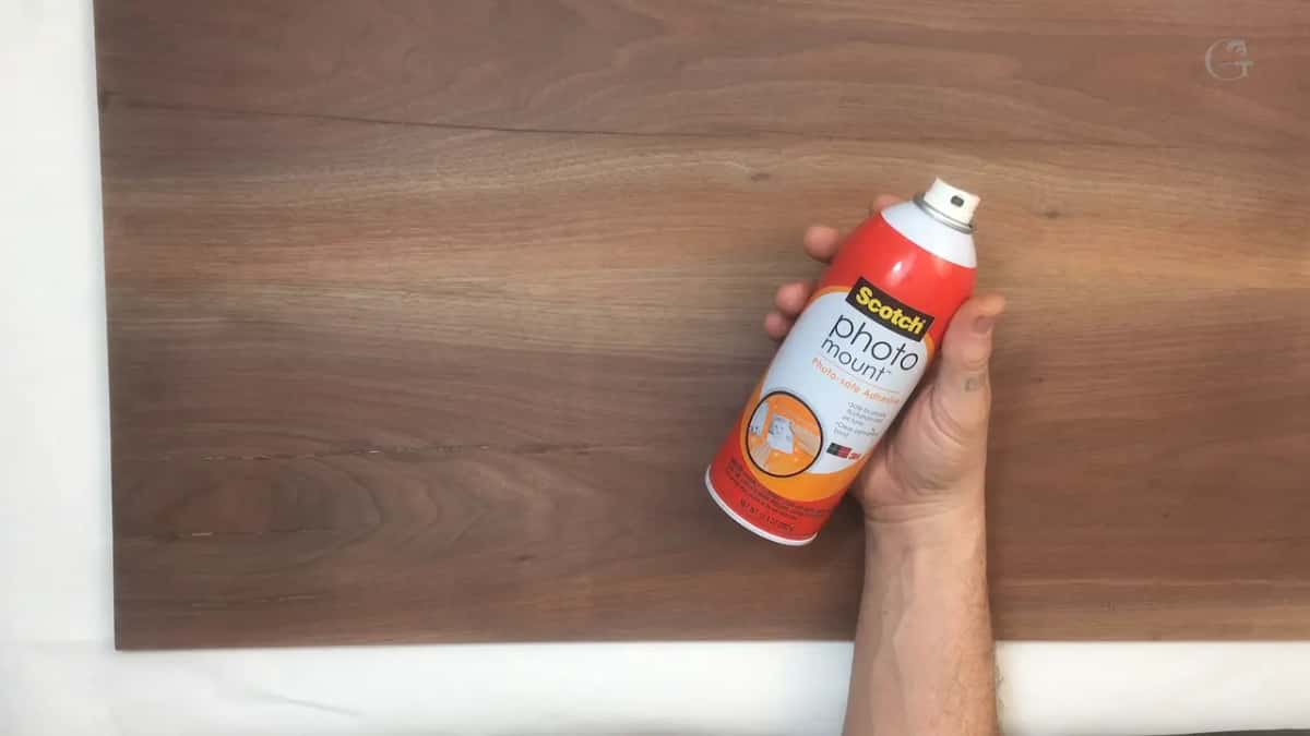 A can of spray adhesive held above a dark board, with white paper spread underneath it.
