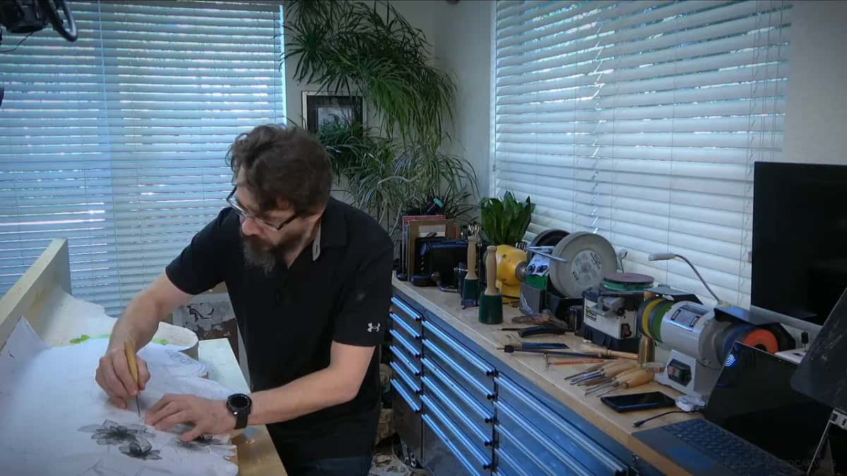 Bent over the bench, he draws onto a big paper sheet where two flowers are already worked out in pencil.