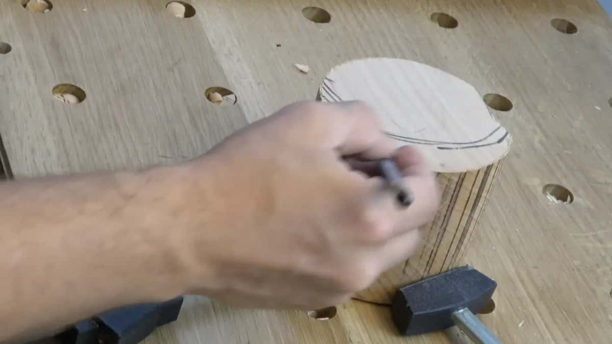 Someone draws an oval on the top of a block held in the bench, with the block side fully visible.
