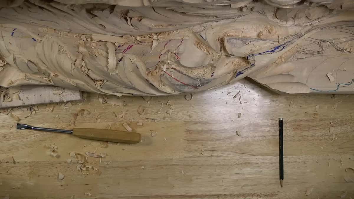 The carved edge of a long panel runs along the top of the frame, with a tool and a pencil below it.