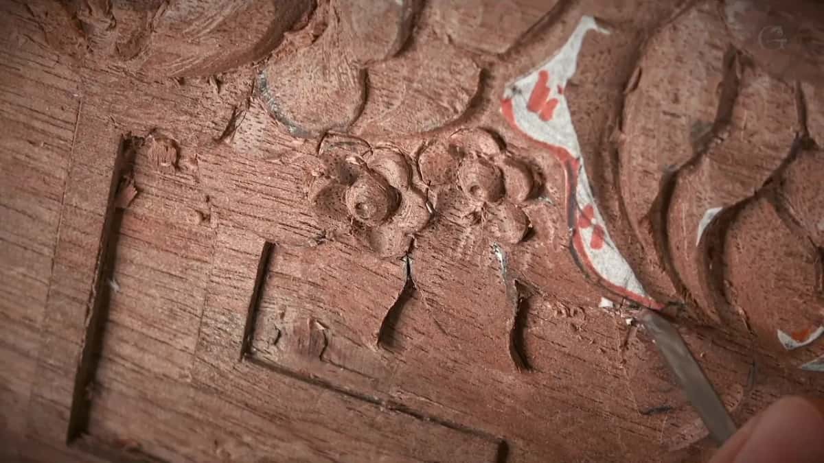 Small flowers and a shallow border are carved barely below the surface of a dark reddish board.