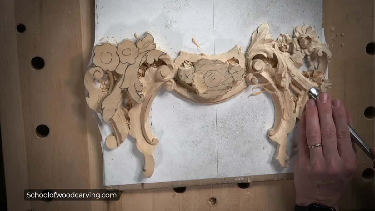 Seen from above, a pale pierced flower and scroll ornament on white paper, a gouge at its edge.