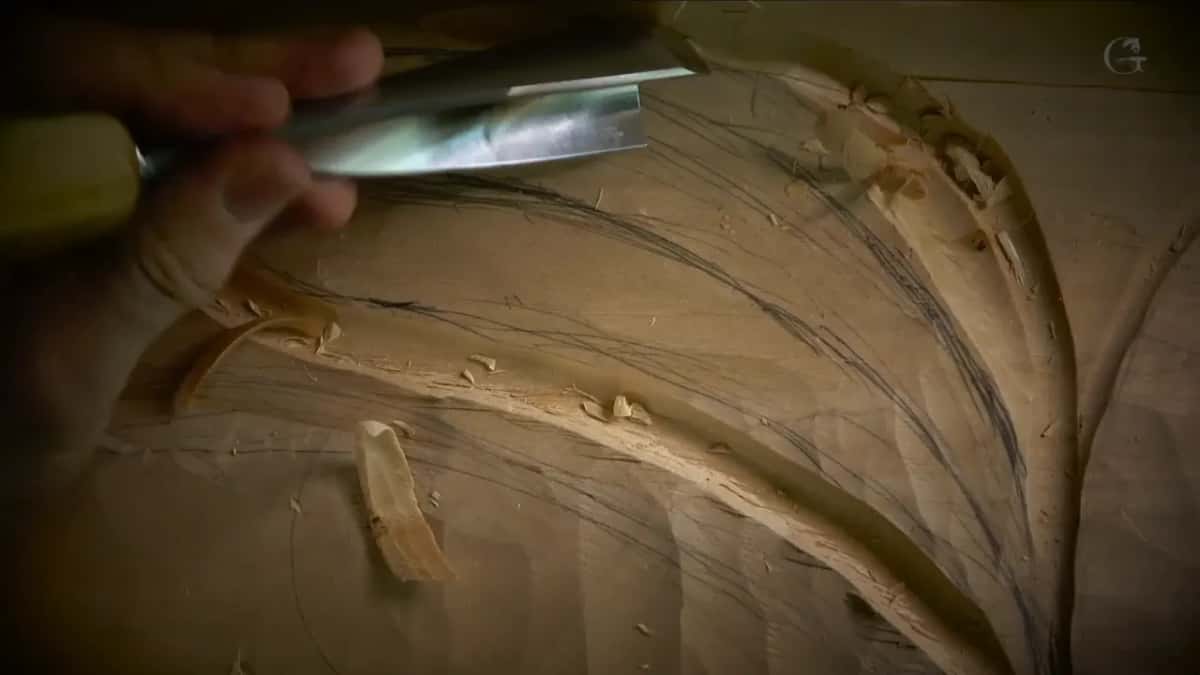 Big steel gouge held flat at the top of the frame over a sweep of pencil marks and fresh curls