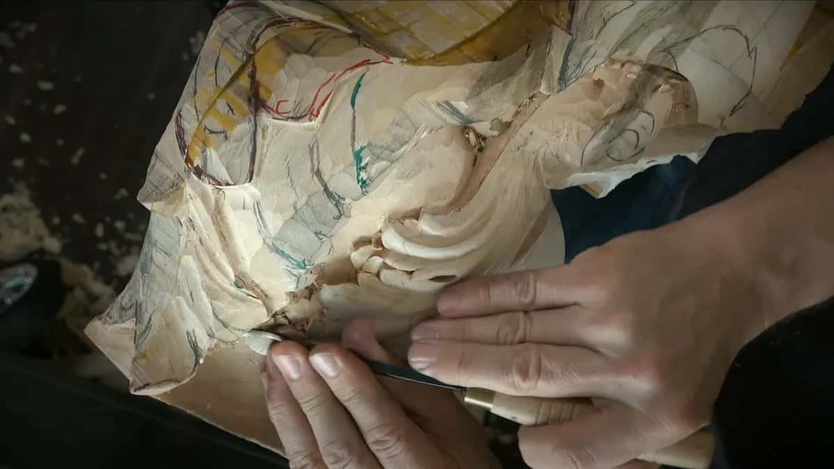 Two hands work a gouge along the base of the leaf, with chips and a round hole just above