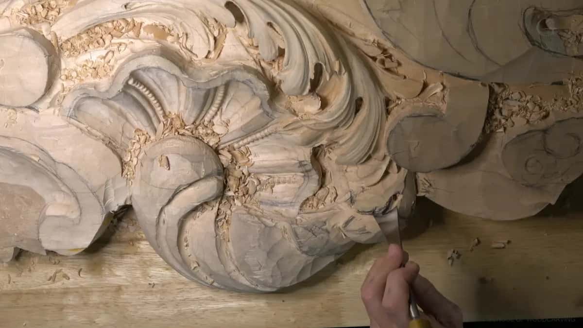 Right hand guides a slim gouge into the crease where a lobe meets the shell, chips scattered around it.