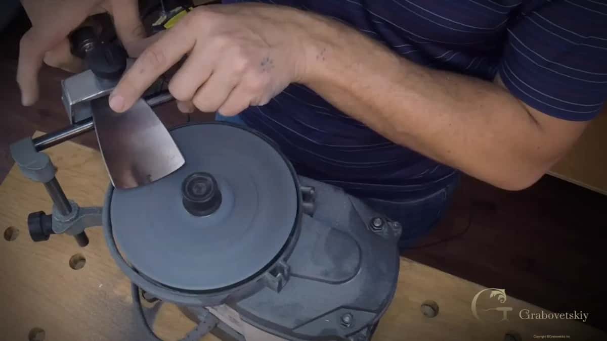 Finger points at the polished bevel while the tool rests over a dark fine disc.