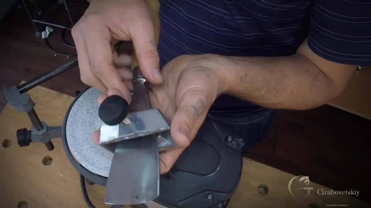 Two hands settle the broad blade into the steel jig.