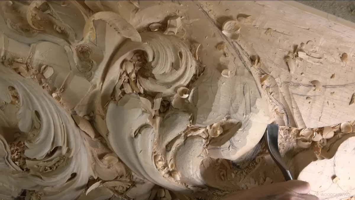 A spoon gouge, its shank curved, dips into the hollow next to the big scroll.