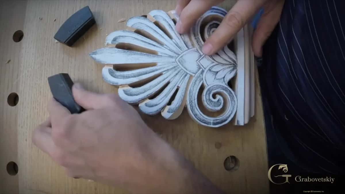 Fingers set a black stop block into one of the bench holes, right beside the sawn fan and its spirals