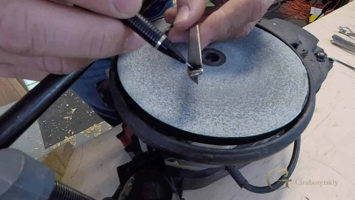 Honing the V tool A V tool held flat against a spinning sharpening disc, both hands steadying the blade