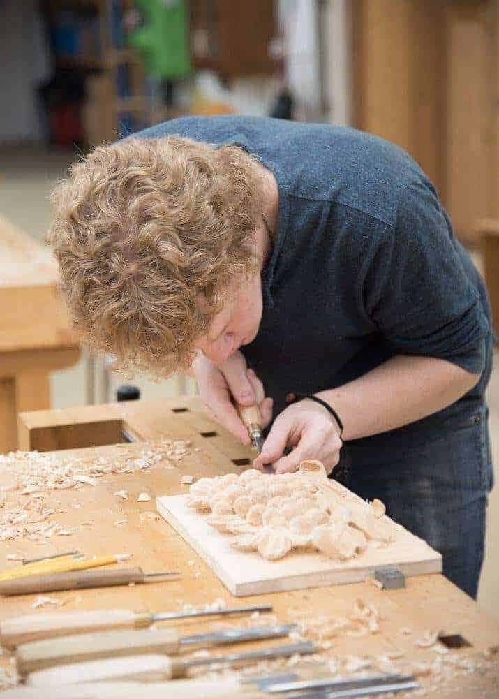 A student at the bench A student bent over a bench working a relief carving, chisels lined up beside the board