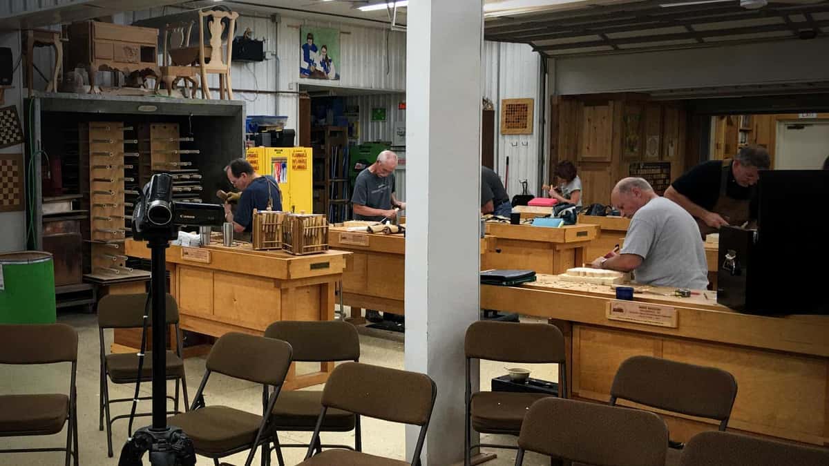 The shop before a class starts Empty teaching shop, benches in rows, carvings on the far wall