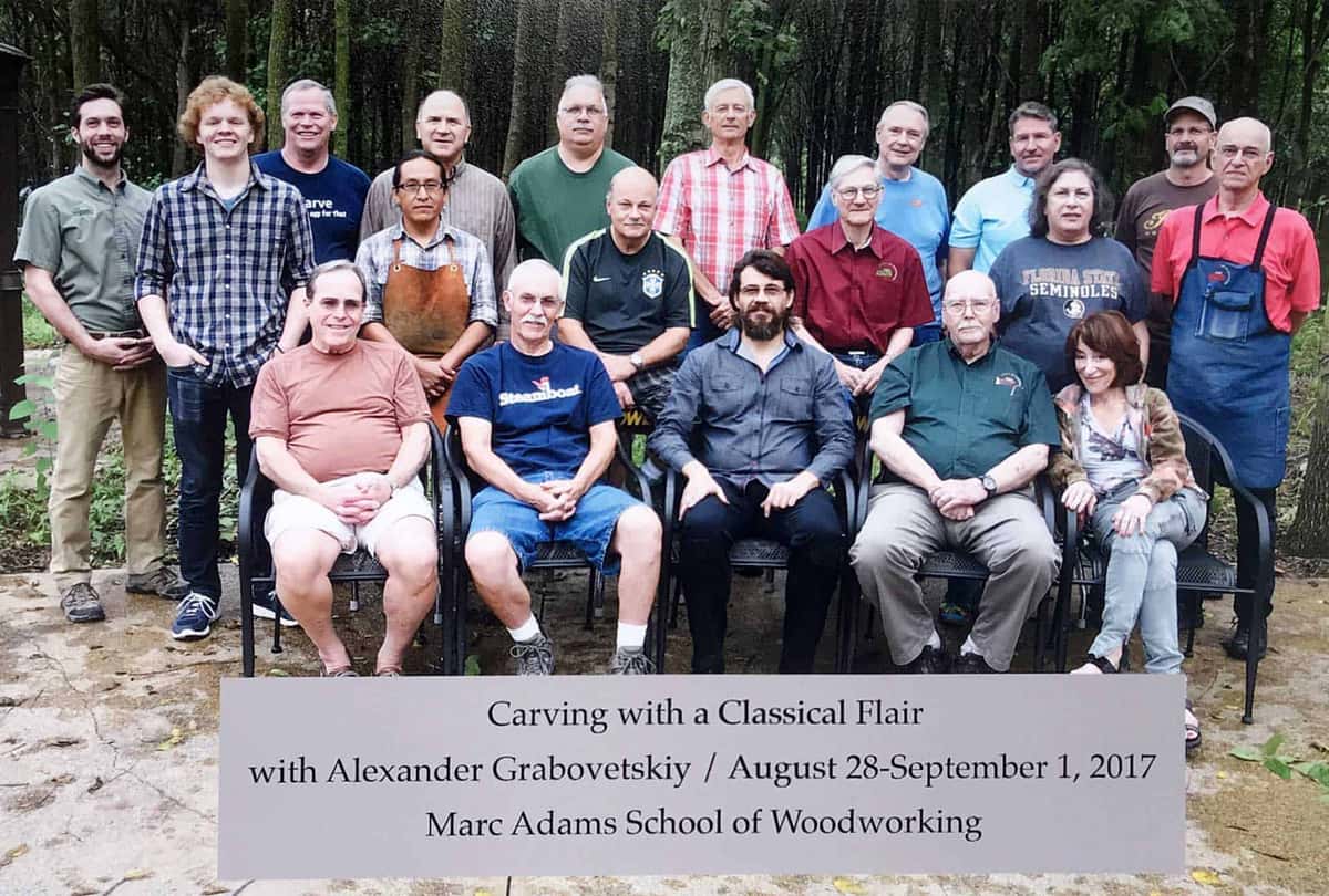 Carving with a Classical Flair, 2017 Class group photo with a printed sign reading Carving with a Classical Flair with Alexander Grabovetskiy, August 2017