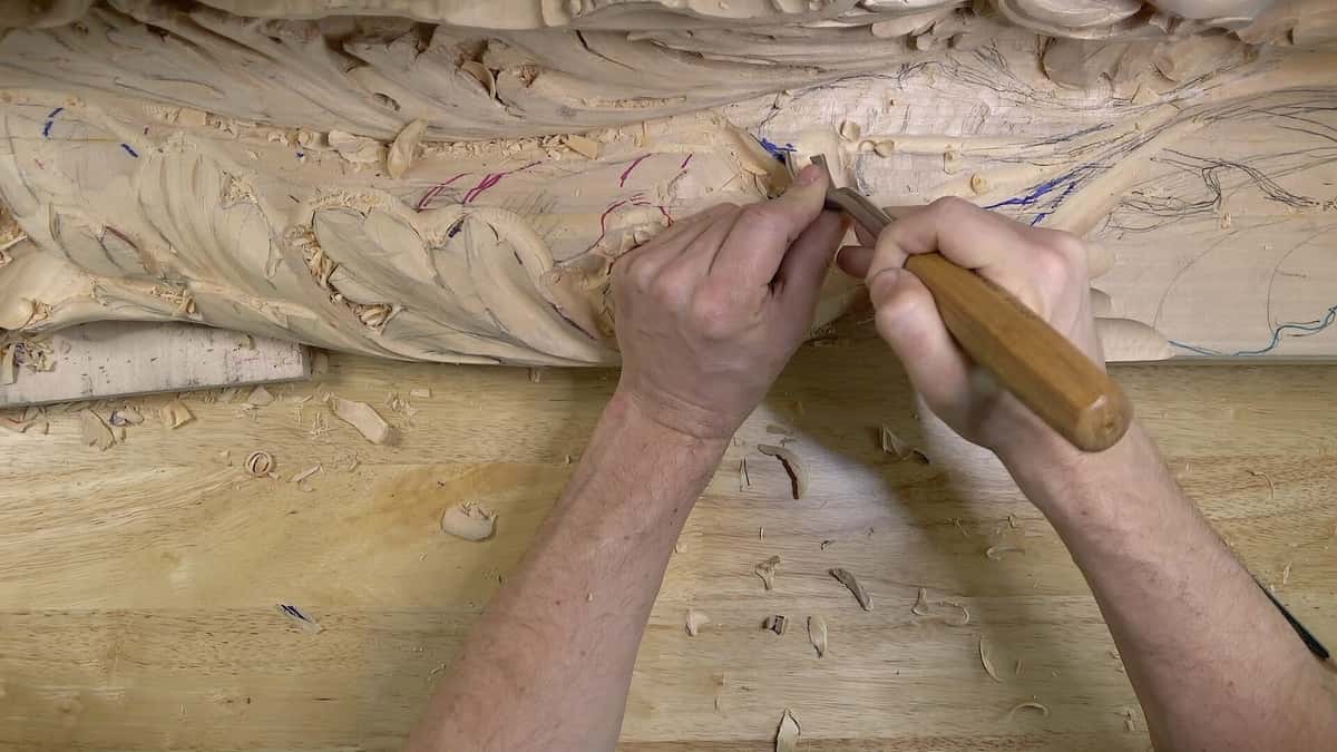 Two hands guiding a gouge through deep basswood foliage