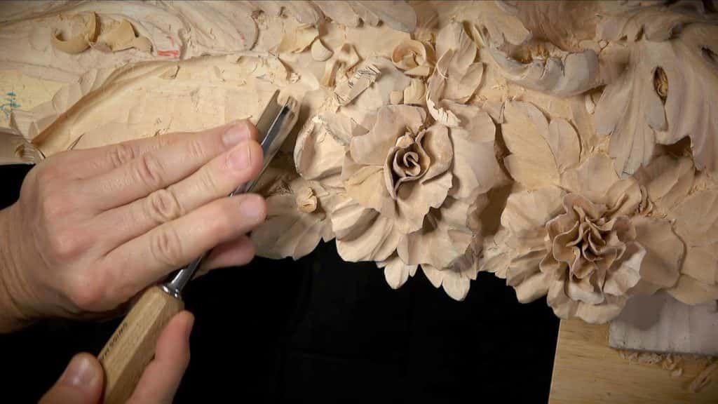 Carving flower designs by hand with a chisel on a Venetian style panel