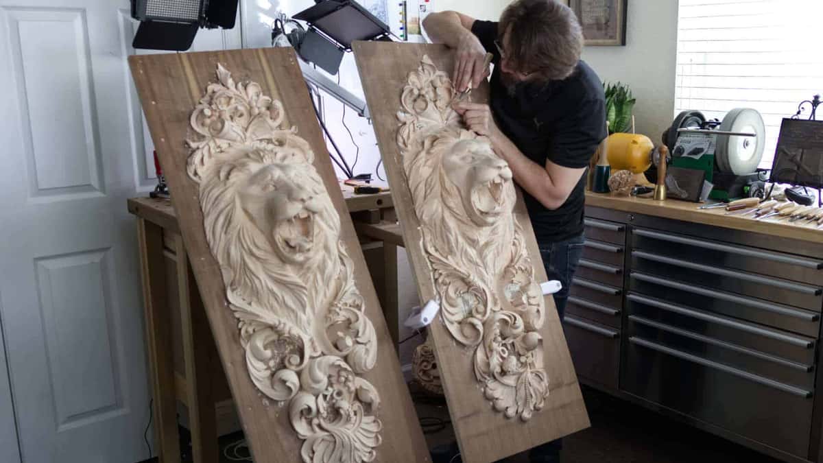 Alexander Grabovetskiy carving a pair of lion head relief panels in his workshop beside a wall of gouges