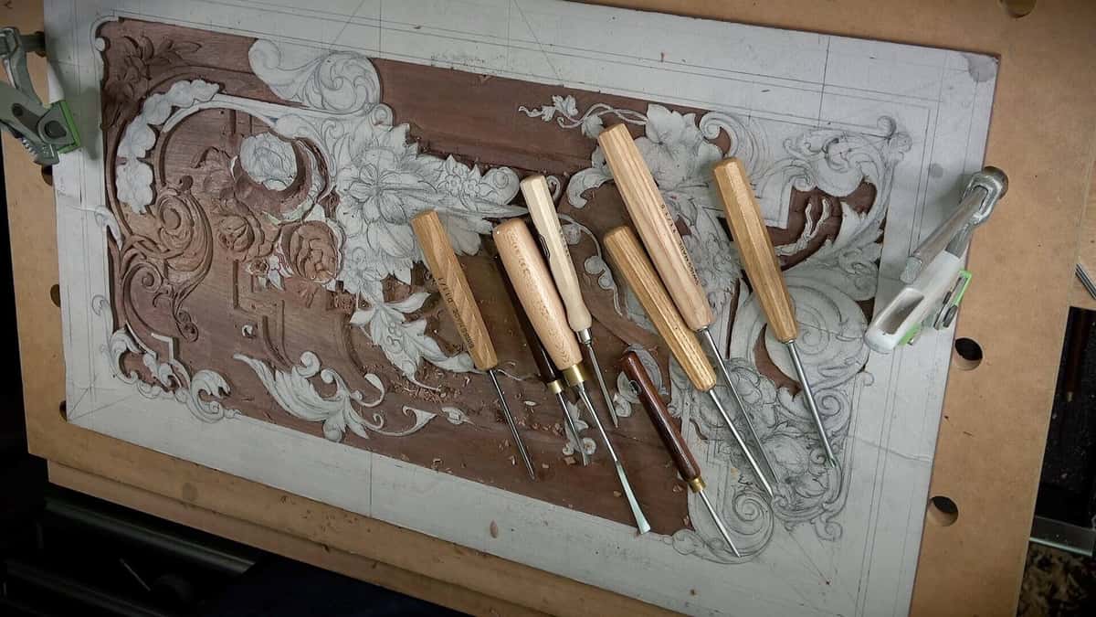 Working drawing glued straight onto a walnut relief panel with six carving gouges lying on top