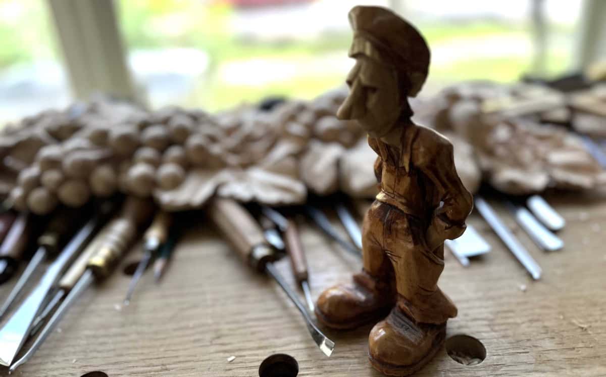 Small carved figure of a man in a flat cap standing before a row of gouges