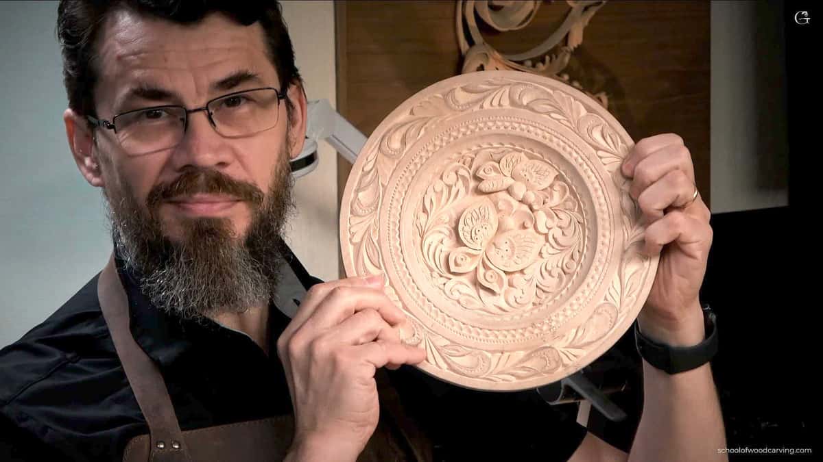 A person holding a beautifully carved wooden plate with floral designs. The individual looks proud of their work, which showcases their skills in wood carving. This image represents the essence of wood carving classes and lessons, inviting others to explore this art form.