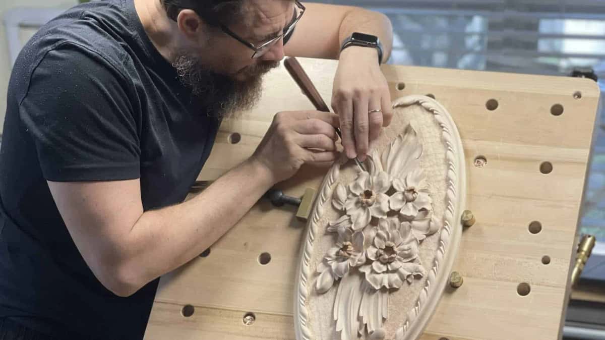 WOODCARVING LESSONS: Woodcarver Grabovetskiy carves flowers and leaves on wood using a chisel, showing woodcarving skills in a bright workspace. - Wood Carving tutorials