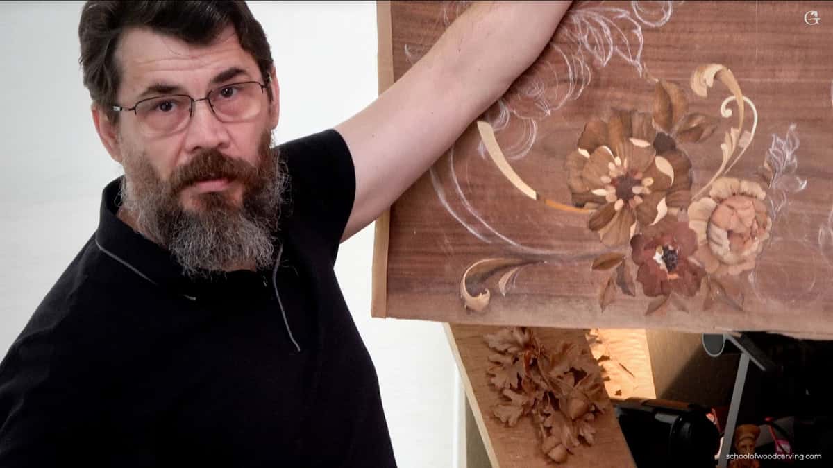 Man with glasses and a beard holding a wooden panel featuring intricate floral carvings and designs.