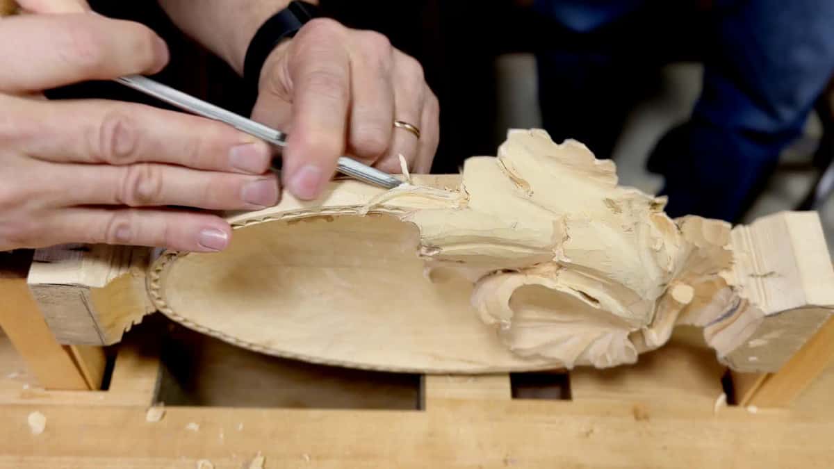 WOODCARVING LESSONS: Woodcarver Grabovetskiy carves detailed shapes into light wood on a workbench using a metal tool for woodcarving lessons. - Wood Carving tutorials