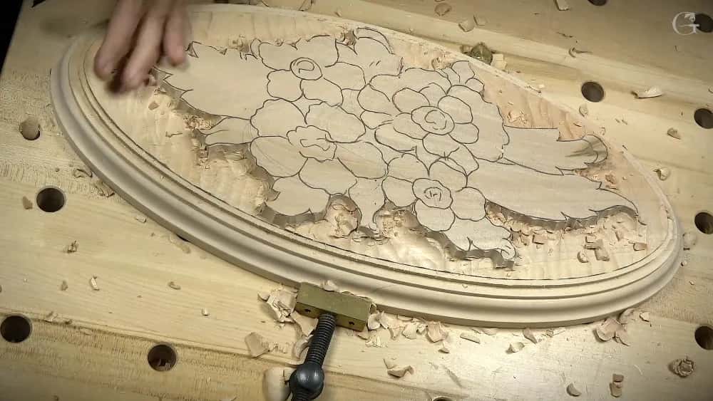 Carver uses a gouge to remove wood chips from a flower relief pattern on an oval plaque