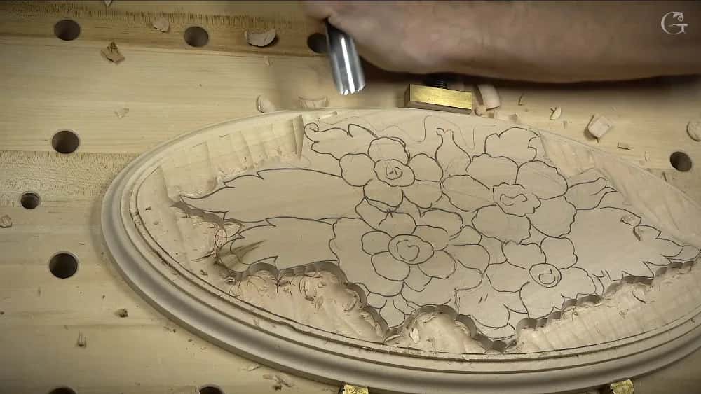 Carved wood relief showing flowers and leaves on an oval panel with tool marks visible