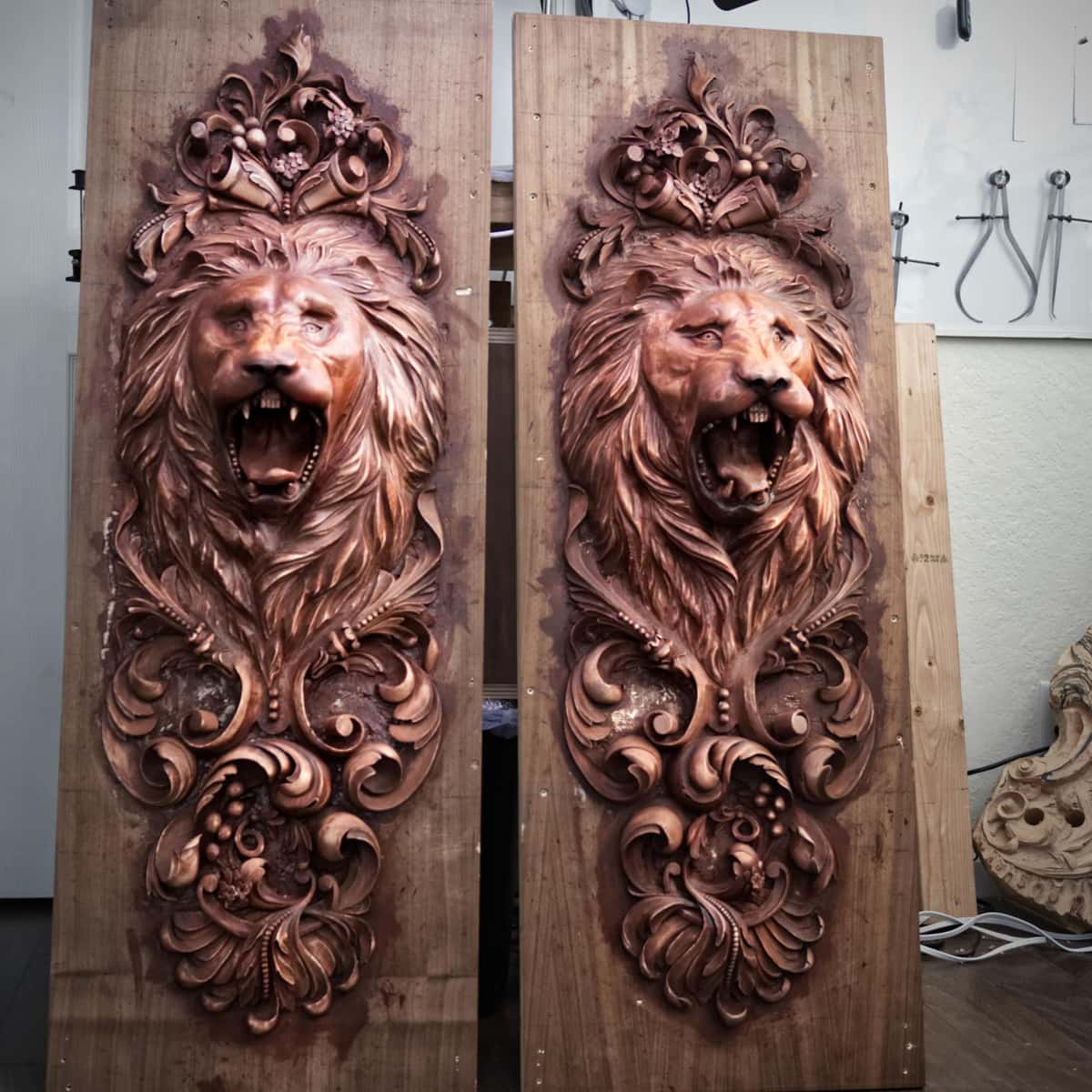 Two tall wood panels show matching relief carvings of roaring lion heads framed by acanthus scrolls