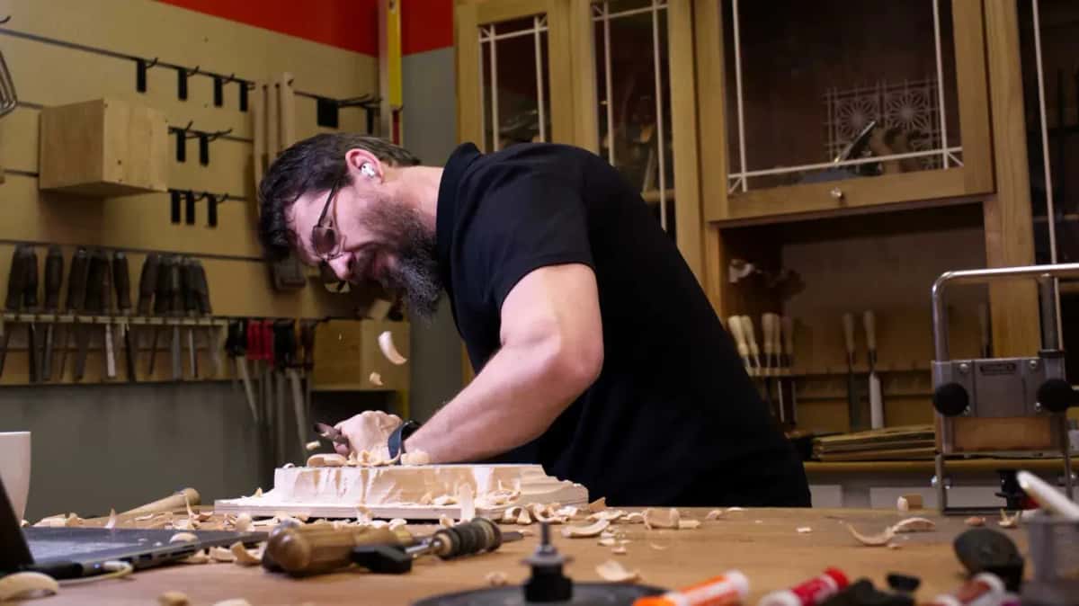 Alexander Grabovetskiy bent over his bench cutting a relief panel, racks of gouges behind him