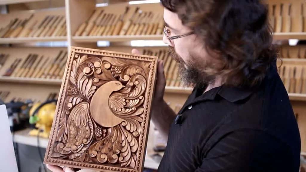 Alexander Grabovetskiy holding the finished board in front of a wall of carving gouges