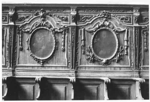 An old photograph of a carved interior, panelled walls and oval frames above the seating