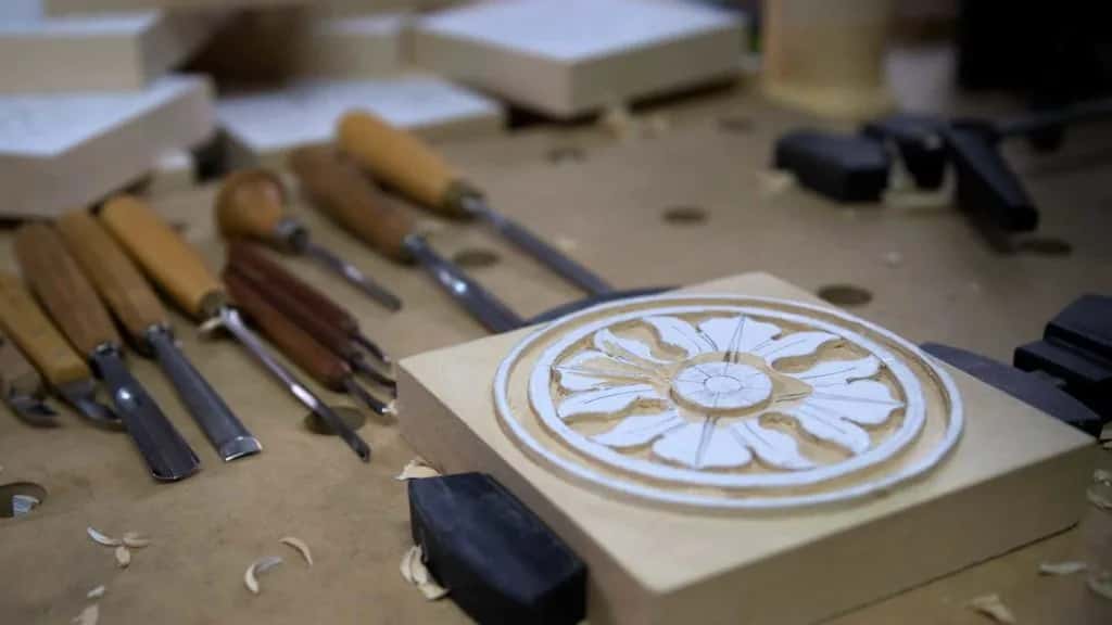An antique style rosette on its block, held down with holdfasts, gouges within reach on the bench