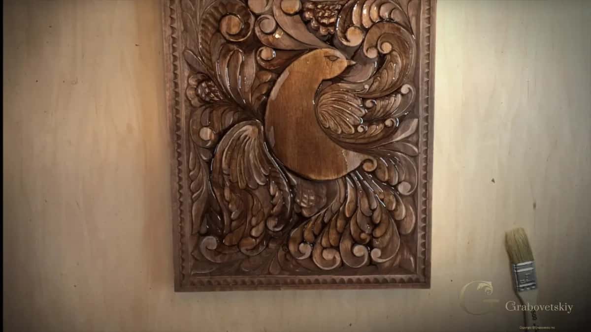 A carved bird panel stained dark brown, lying on a pale bench top.