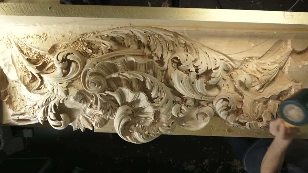 A long pale frieze carved in deep leaf scrolls, chips banked up along the whole length of the board.
