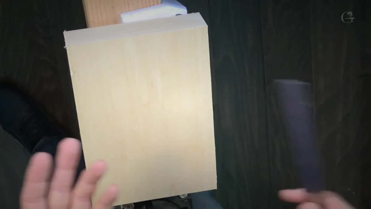 A pale block held up in front of a dark stained board.