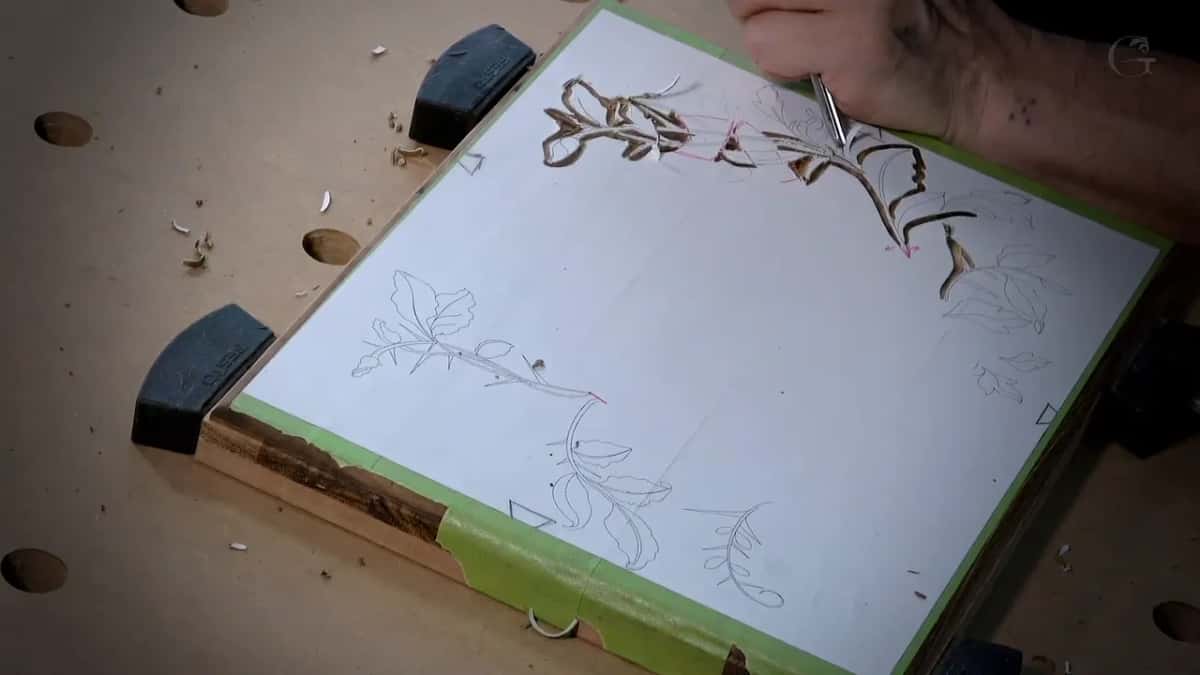 A white paper pattern taped to a dark board, its top corner already carved through to brown leaves.