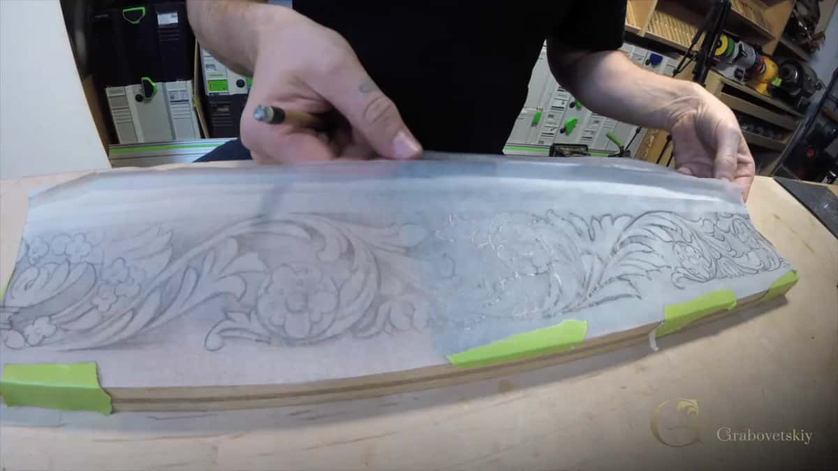 Hands lift tracing paper off a pale curved board, green tape still holding the drawing in place.
