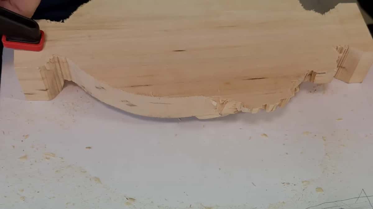 A pale blank sawn to a scalloped outline, clamped in sawdust.