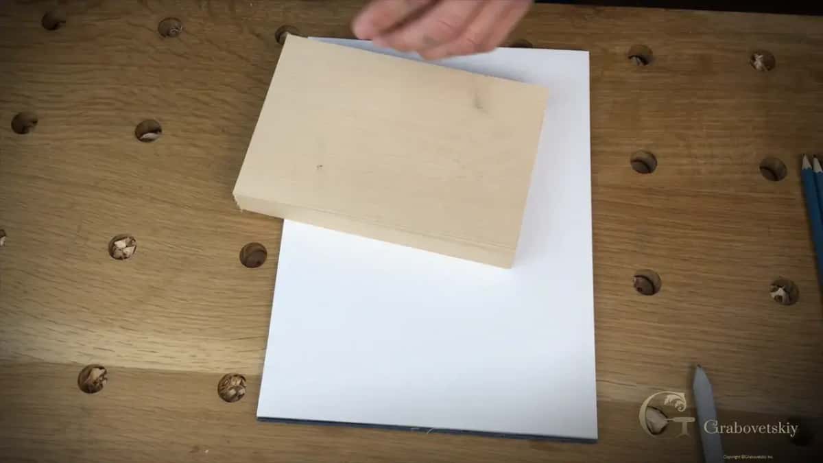 Pale basswood block sitting on a white paper pad on an oak bench with plugged dog holes and pencils nearby